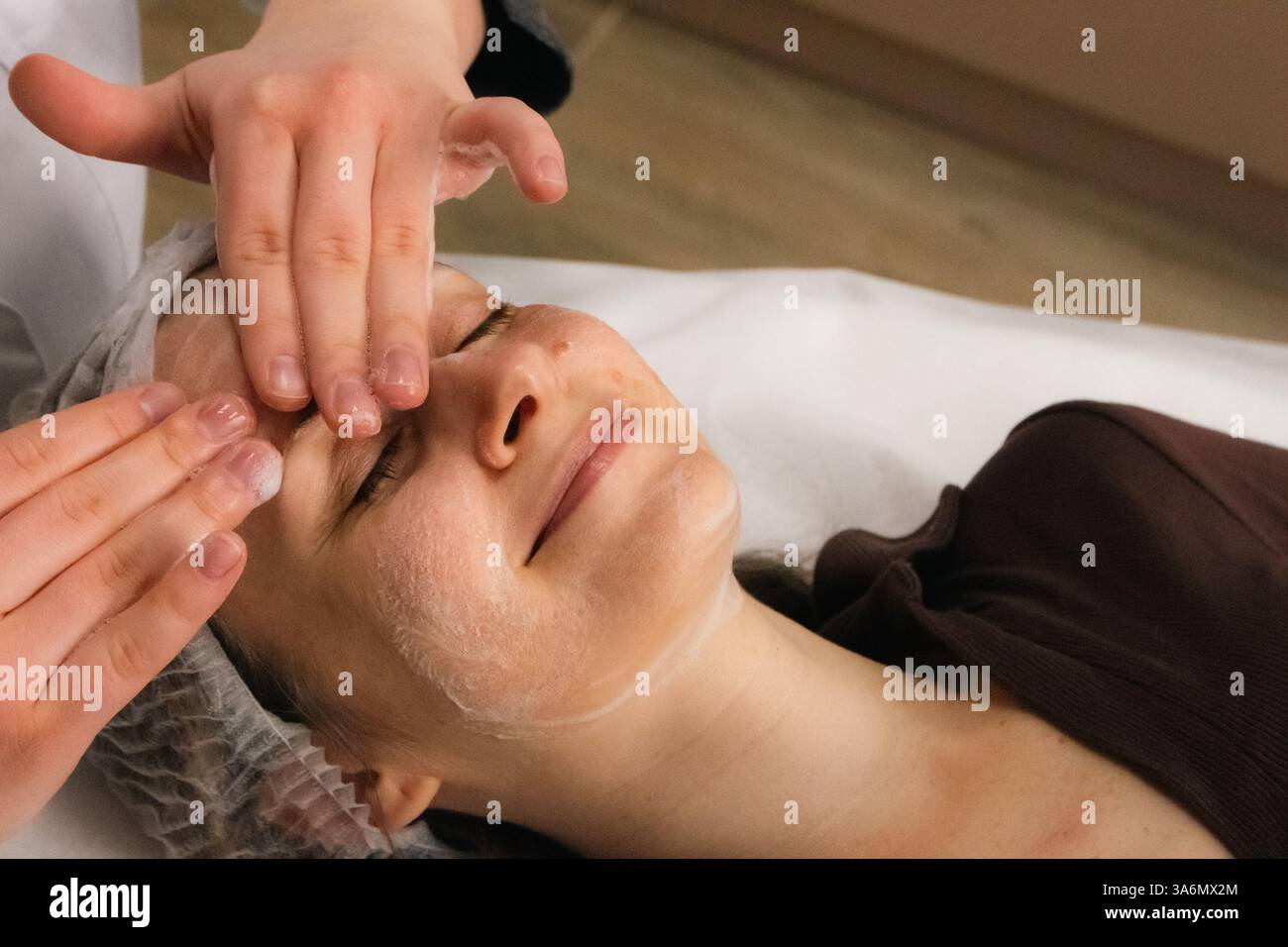 Pulizia della schiuma e massaggio viso nel salone di bellezza. Donna sorridente che si rilassa con un massaggio anti-età. Procedura di benessere. Trattamento per la cura della pelle. Foto Stock