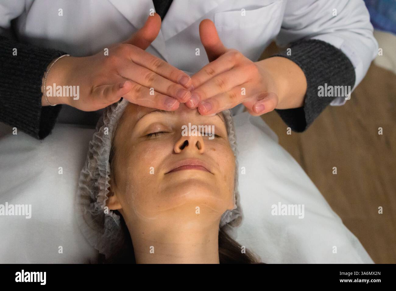 Pulizia della schiuma e massaggio viso nel salone di bellezza. Donna sorridente che si rilassa con un massaggio anti-età. Procedura di benessere. Trattamento per la cura della pelle. Foto Stock