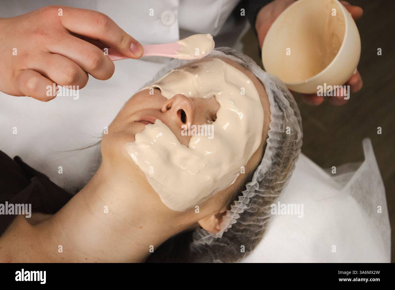 Maschera di alginato sul viso di donna in salone di bellezza. Donna rilassante con maschera anti-invecchiamento. Cosmetologo che mette maschera alginata con spatola sul viso. Foto Stock