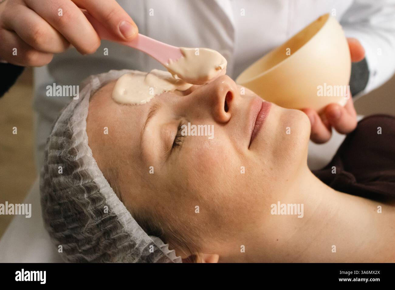 Maschera di alginato sul viso di donna in salone di bellezza. Donna rilassante con maschera anti-invecchiamento. Cosmetologo che mette maschera alginata con spatola sul viso. Foto Stock