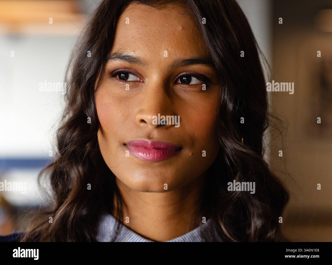 Donna sicura di sé con capelli ondulati che guarda lontano e pensa in un ufficio moderno Foto Stock