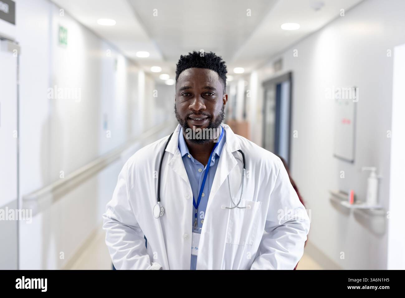 Medico nel corridoio dell'ospedale che indossa il cappotto bianco e lo stetoscopio, sorridendo con fiducia Foto Stock