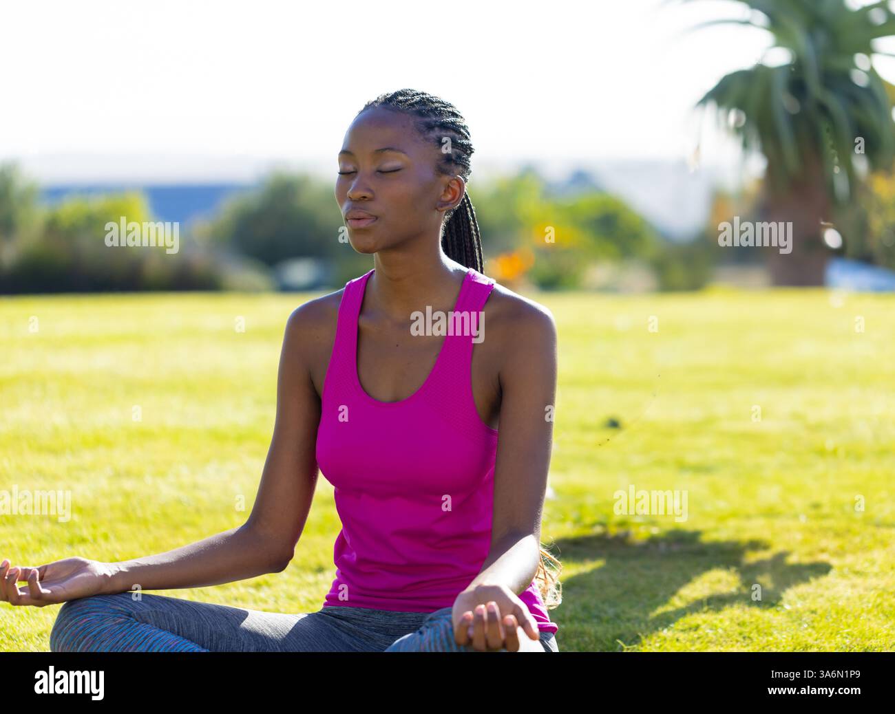 Donna afroamericana che meditava sull'erba nel cortile, godendosi momenti di pace Foto Stock