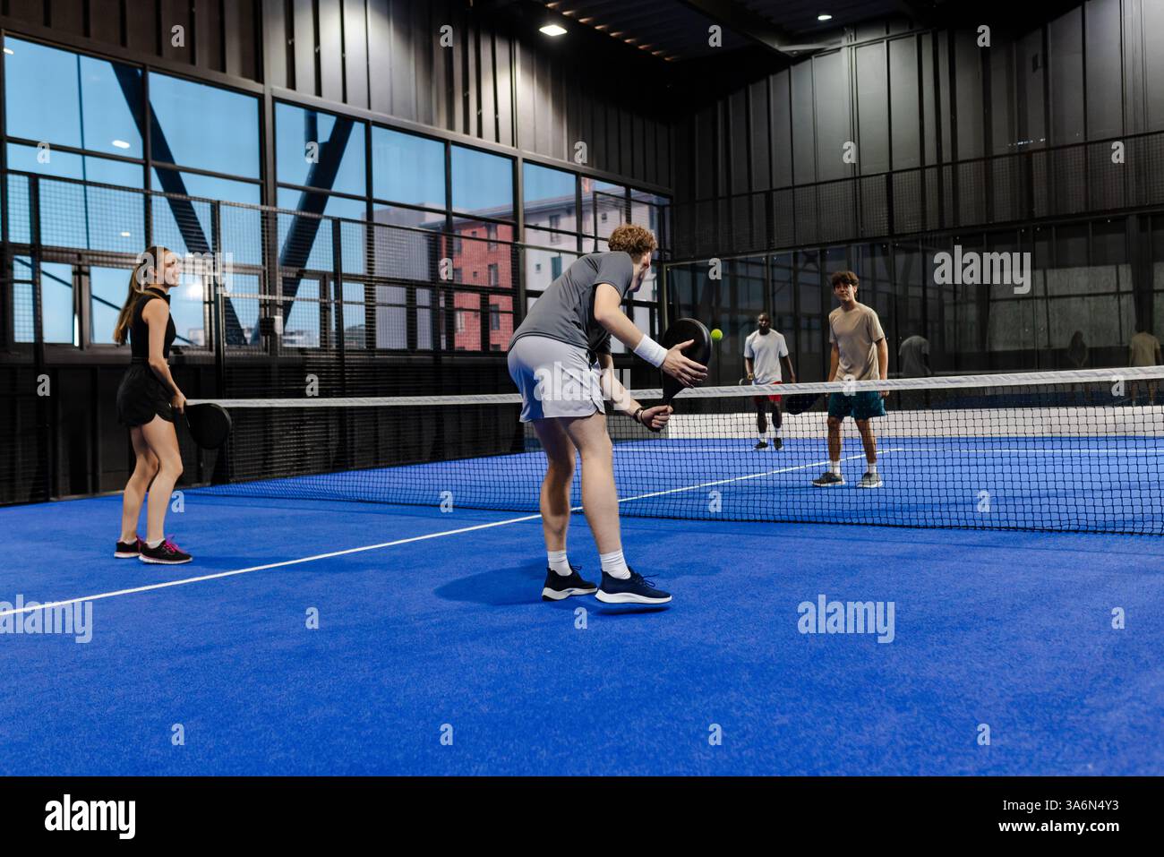 Giocando in gruppo al padel tennis al chiuso, concentrandosi sul lavoro di squadra e sulla strategia Foto Stock