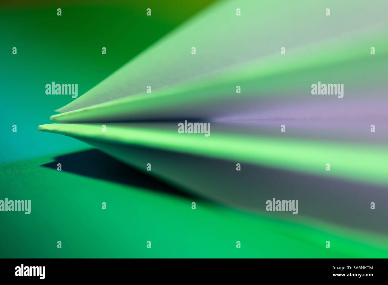 Una vista dettagliata della carta piegata mostra bordi e strati lisci. I colori si fondono delicatamente su uno sfondo verde brillante, evidenziando la texture Foto Stock