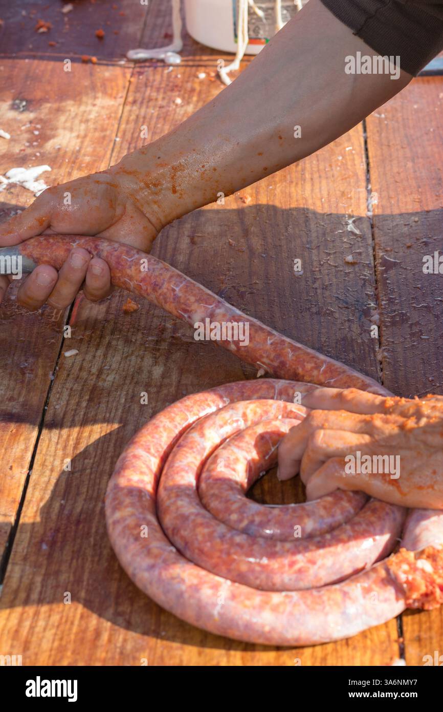Immagine ravvicinata che raffigura il processo di produzione manuale della salsiccia, maneggiando le mani la salsiccia cruda su una superficie di legno. Foto Stock