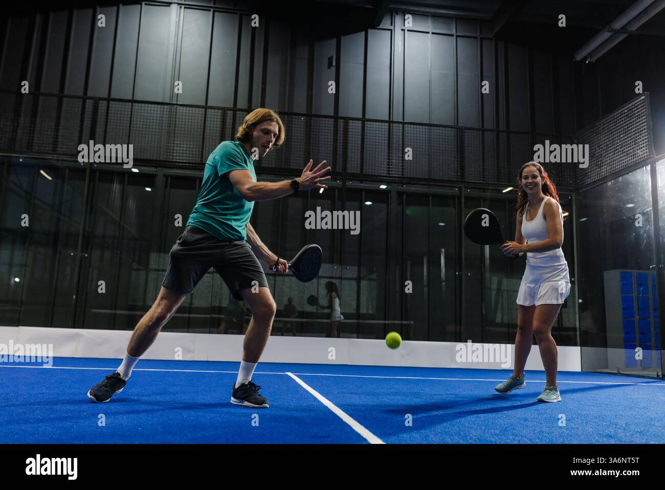 Giocando a tennis a padel, con un uomo concentrato e una donna sorridente che si diverte a giocare al coperto Foto Stock