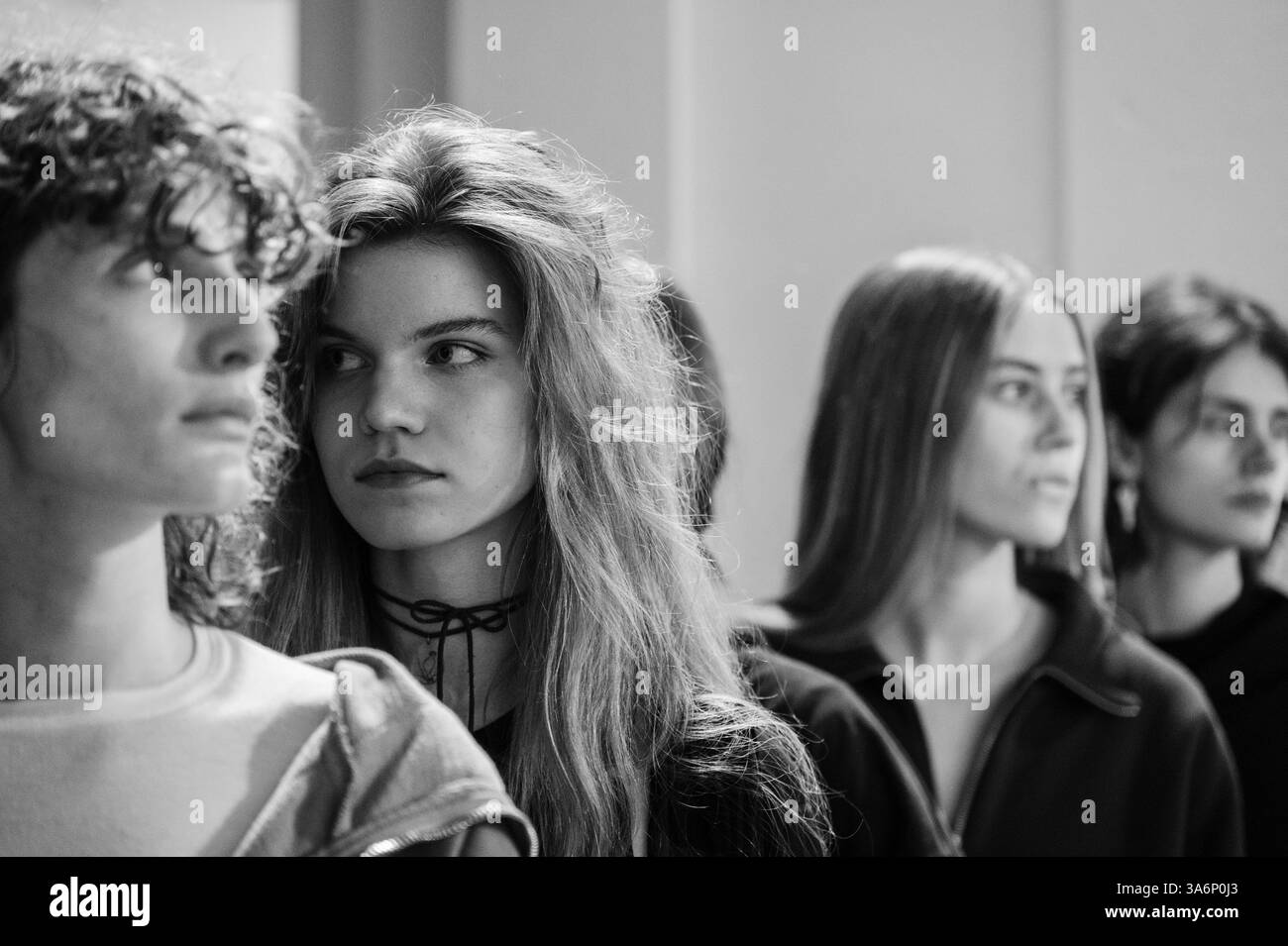Kiev, Ucraina - 14 febbraio 2025: I modelli attendono con impazienza il loro turno mentre gli stilisti modificano abiti e trucco in una vivace area dietro le quinte. Risate e chiacchiere nervoso creano un'atmosfera vivace. Foto Stock