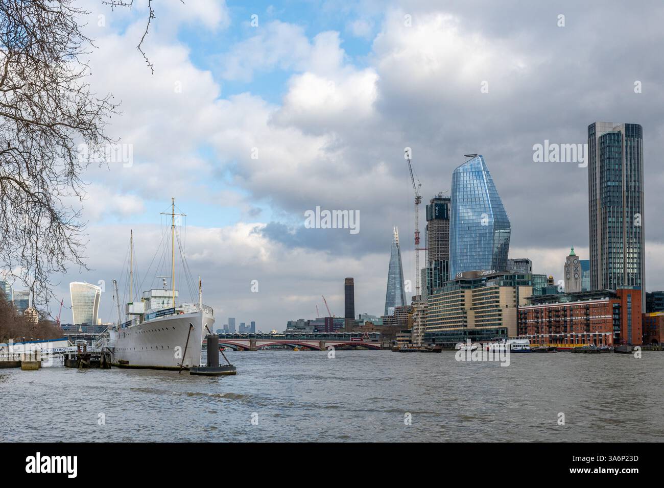 Il Tamigi e lo skyline della città di Londra, visti da Victoria Embankment, Londra, Inghilterra, Regno Unito, con la HMS Wellington, uno sloop in pensione Foto Stock