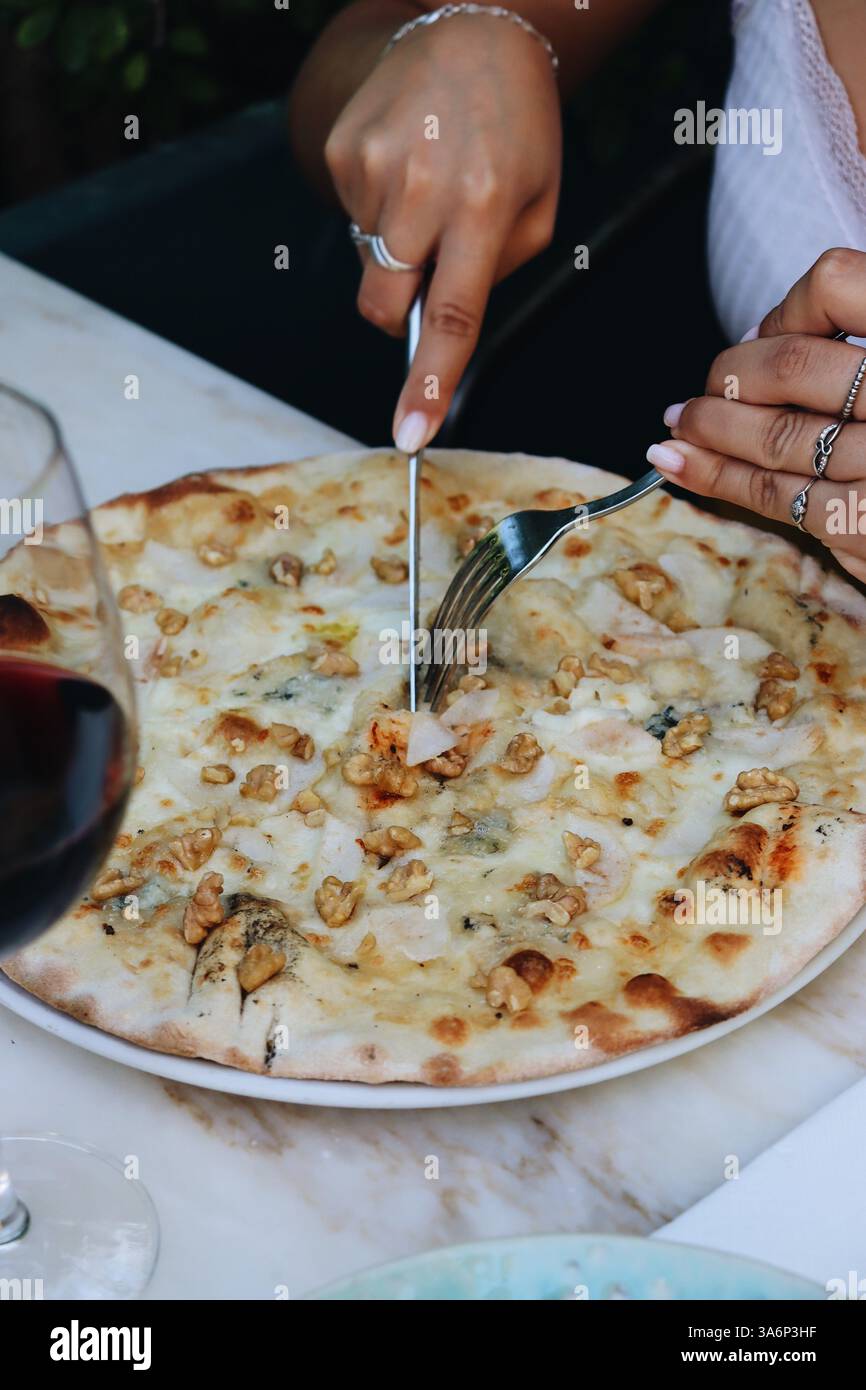 Quattro pizze bianche al formaggio tagliate da mani femminili su un contesto di ristorante, vino rosso su un lato. Vibrazioni per il pranzo Foto Stock
