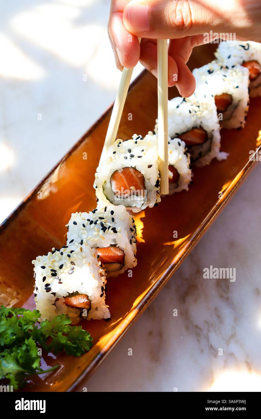 vassoio di sushi maki di salmone e una mano che tiene le bacchette raccogliendone una Foto Stock