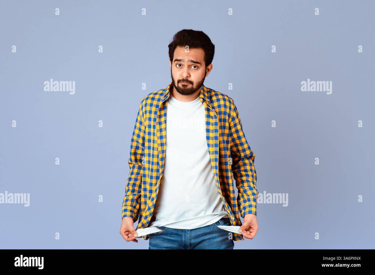 Fallimento e disoccupazione. Uomo indiano sconvolto che mostra tasche vuote su sfondo lilla Foto Stock