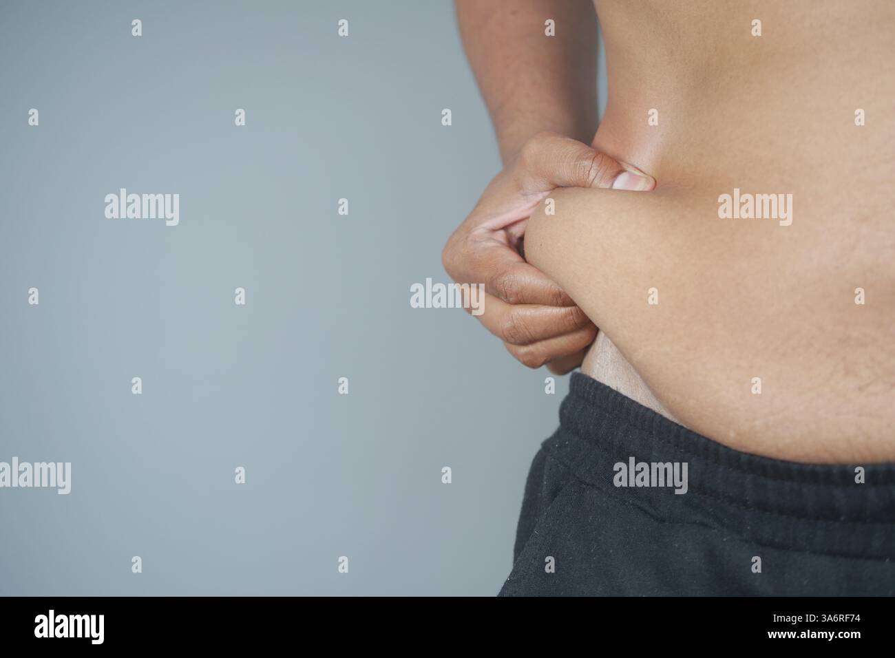Persona che pizzica l'addome per valutare i livelli di grasso corporeo in ambiente privato Foto Stock