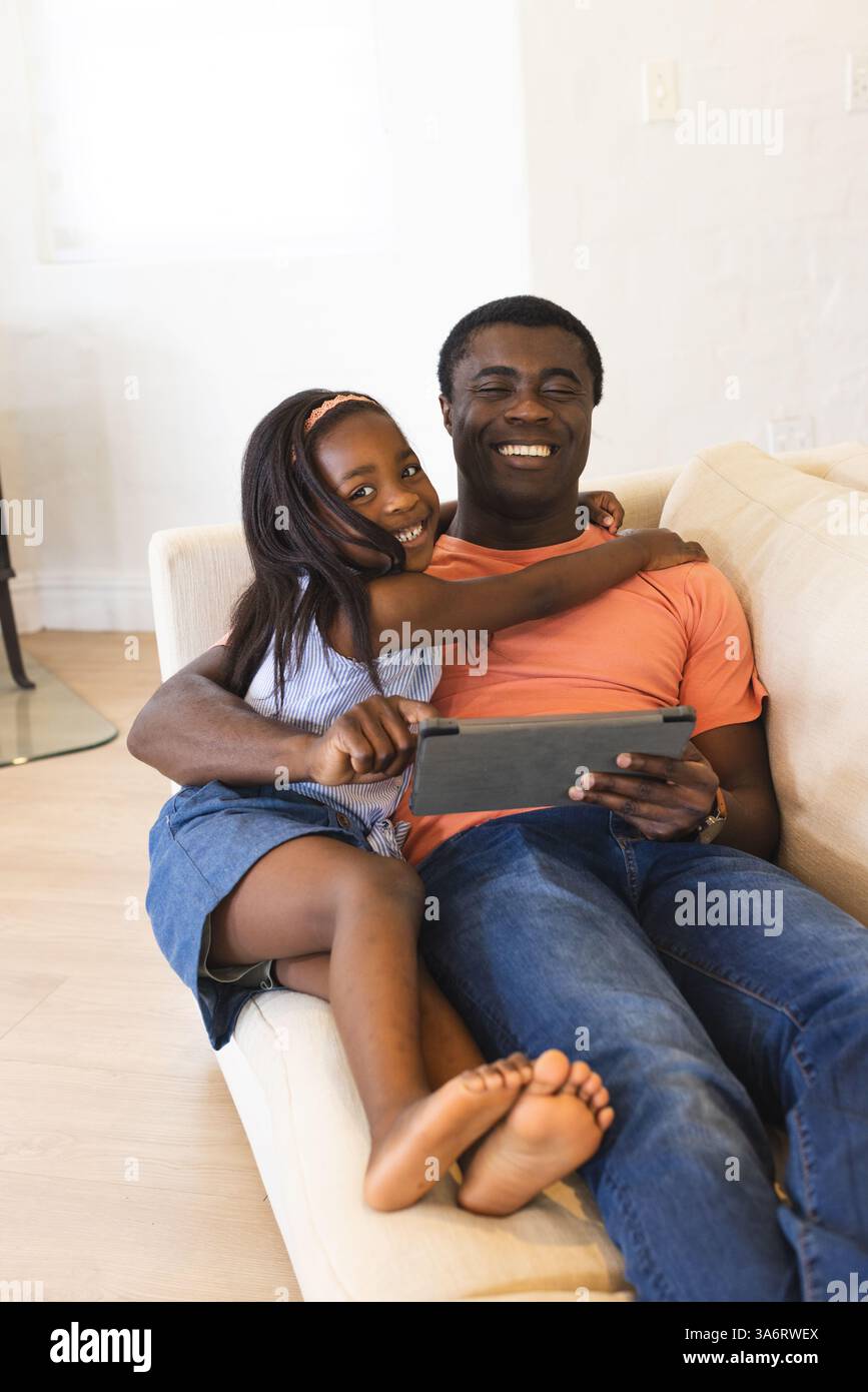 Padre e figlia si godono momenti di qualità insieme sul divano con un tablet Foto Stock