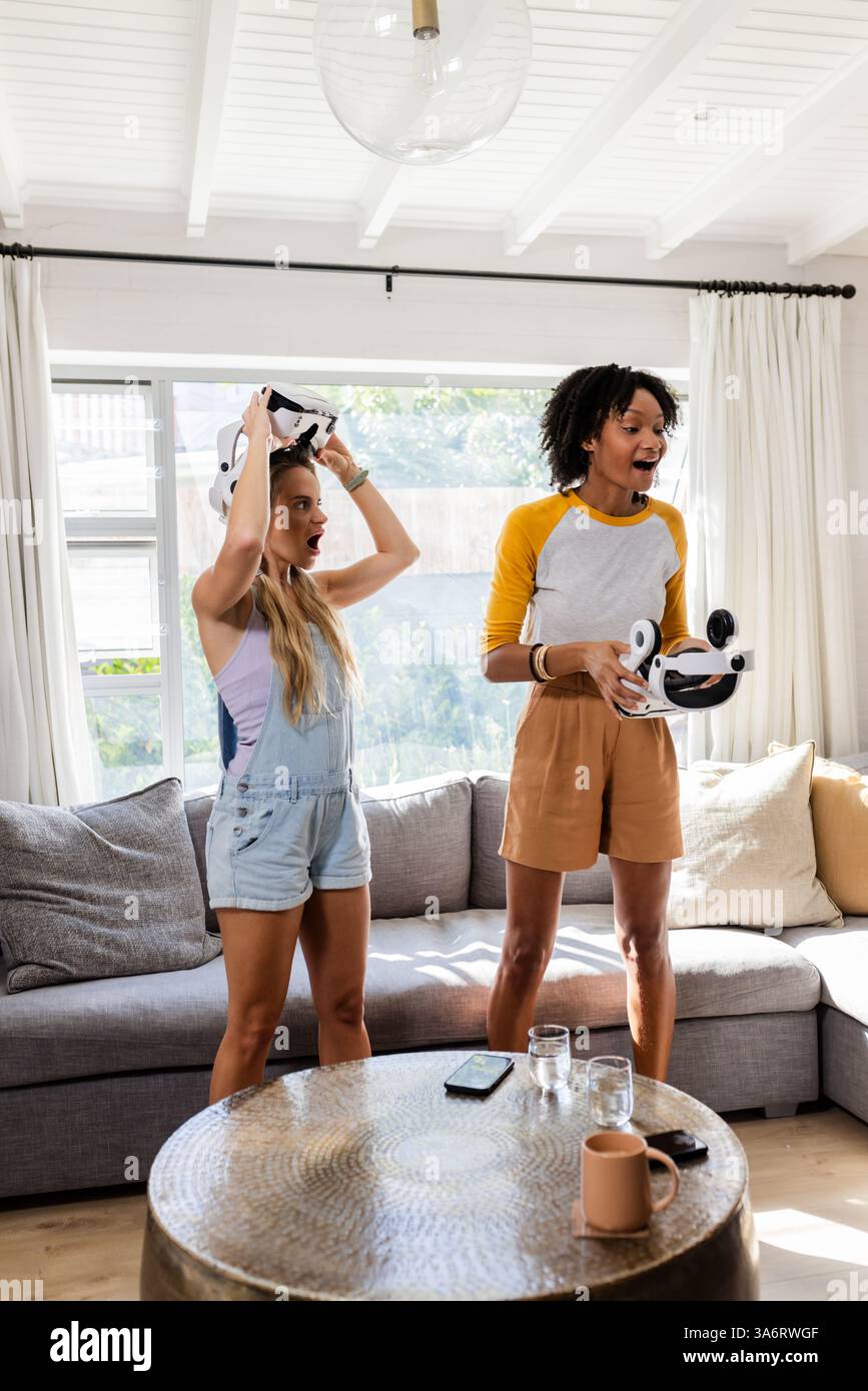 Amici femminili che giocano in realtà virtuale insieme in un accogliente salotto Foto Stock