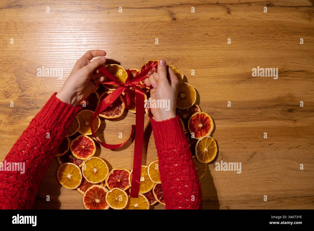 Fase 3 processo fai-da-te di una donna che lega il nastro di Natale con arance secche e pompelmo. Serie di istruzioni artigianali. Decorazioni ecologiche per le vacanze invernali a zero sprechi. Anno nuovo Foto Stock