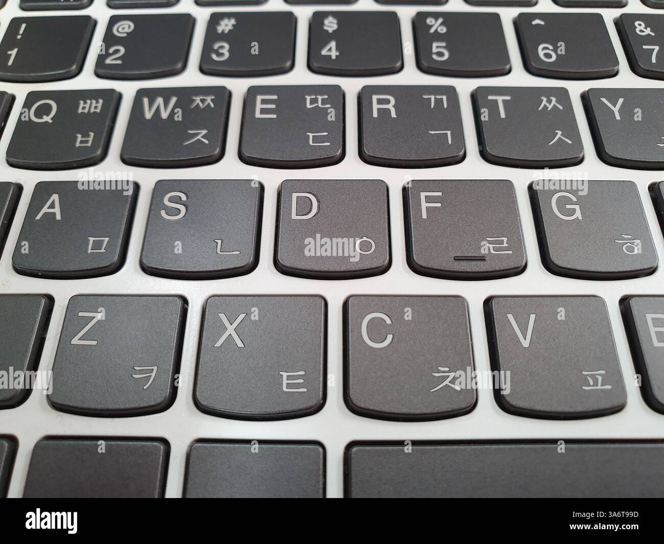 Primo piano di una tastiera per laptop con tasti neri e base bianca, con caratteri inglesi (QWERTY) e coreani (Hangul). Foto Stock