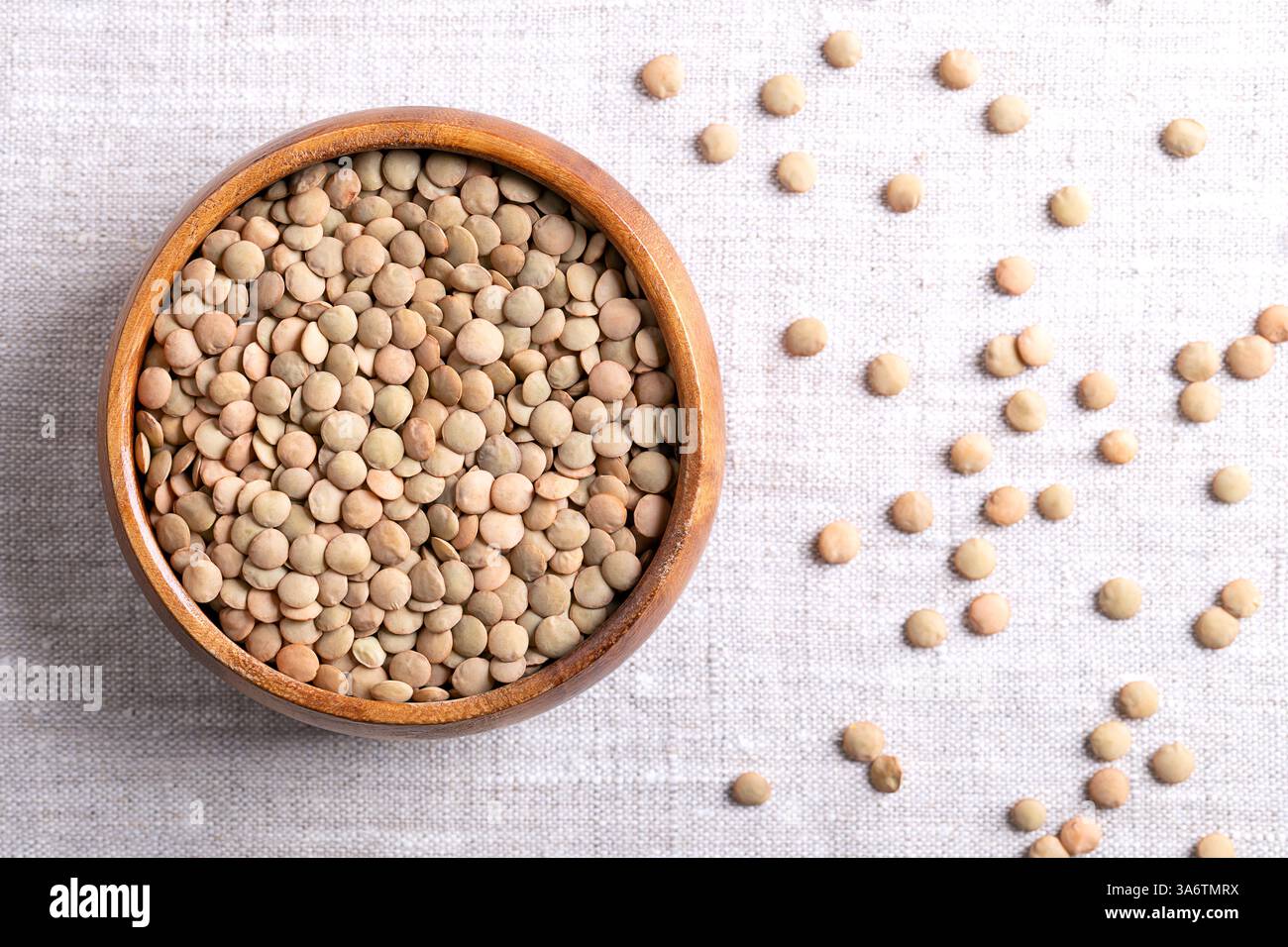 Grandi lenticchie verdi in una ciotola di legno su tessuto di lino. Lenticchie in lastre secche non sgusciate, una varietà di lenticchie piane tipicamente più ampia. Foto Stock