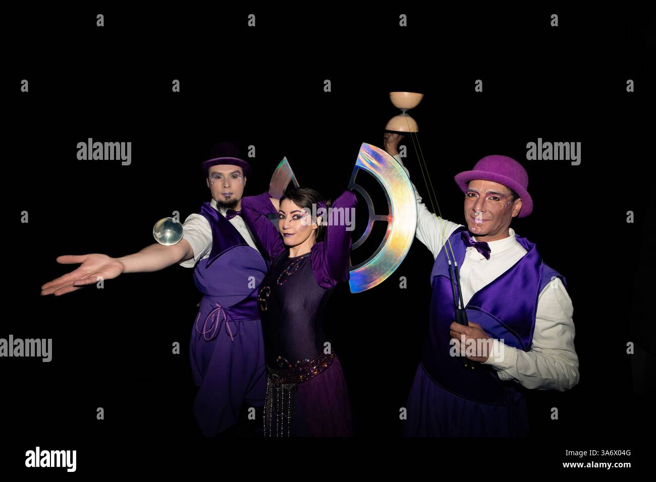 Tre artisti circensi giocheranno e bilancieranno oggetti di scena in uno spettacolo accattivante su uno sfondo nero Foto Stock Tre artisti circensi giocheranno e bilancieranno oggetti di scena in uno spettacolo accattivante su uno sfondo nero Foto Stock