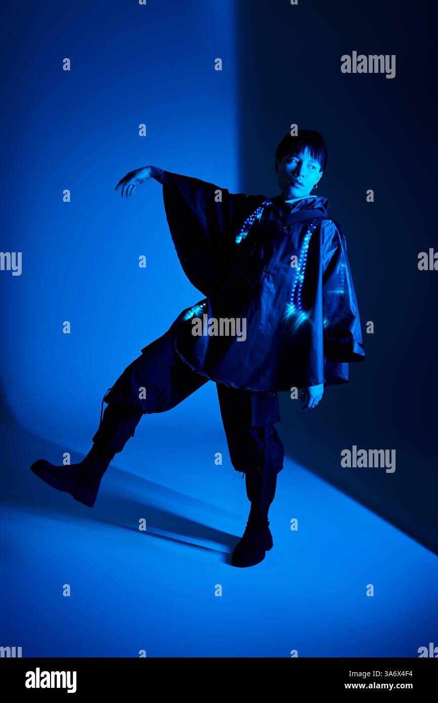 Un giovane ed elegante uomo asiatico indossa un abito moderno sotto luci blu. Foto Stock