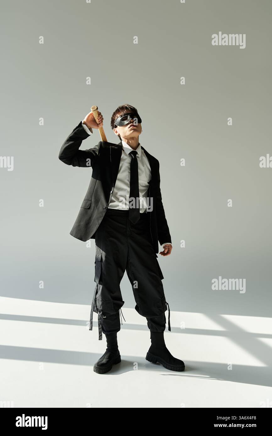 Il giovane asiatico che indossa una tuta si mette in posa sicura mentre tiene in mano un accessorio elegante. Foto Stock