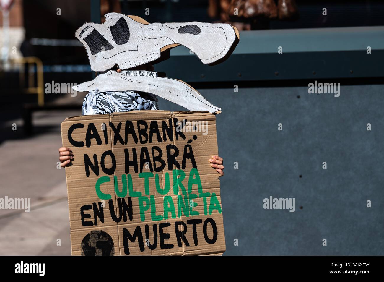Madrid, Spagna. 26 marzo 2025. Attivista per il clima del gruppo Extinction Rebellion che indossa la maschera di dinosauro protesta di fronte alla mostra dei dinosauri della Patagonia al CaixaForum per denunciare che il gruppo CaixaBank continua ad aumentare i suoi investimenti nell'industria dei combustibili fossili. La protesta è condotta in concomitanza con la giornata mondiale del clima. Crediti: Marcos del Mazo/Alamy Live News Foto Stock