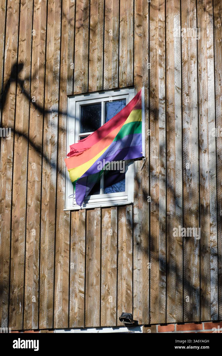 Una bandiera arcobaleno ondeggia da una finestra in un vecchio mulino ad acqua in legno, simboleggiando la diversità e l'inclusione in un ambiente rurale. Foto Stock