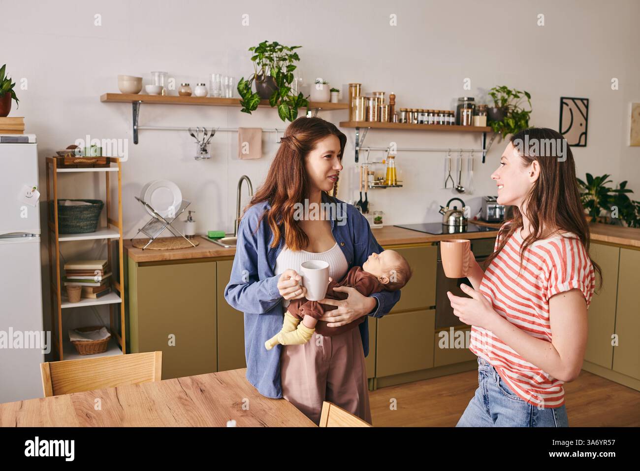 Due madri amorevoli condividono un momento di gioia con il loro bambino nella calda cucina il giorno della mamma. Foto Stock