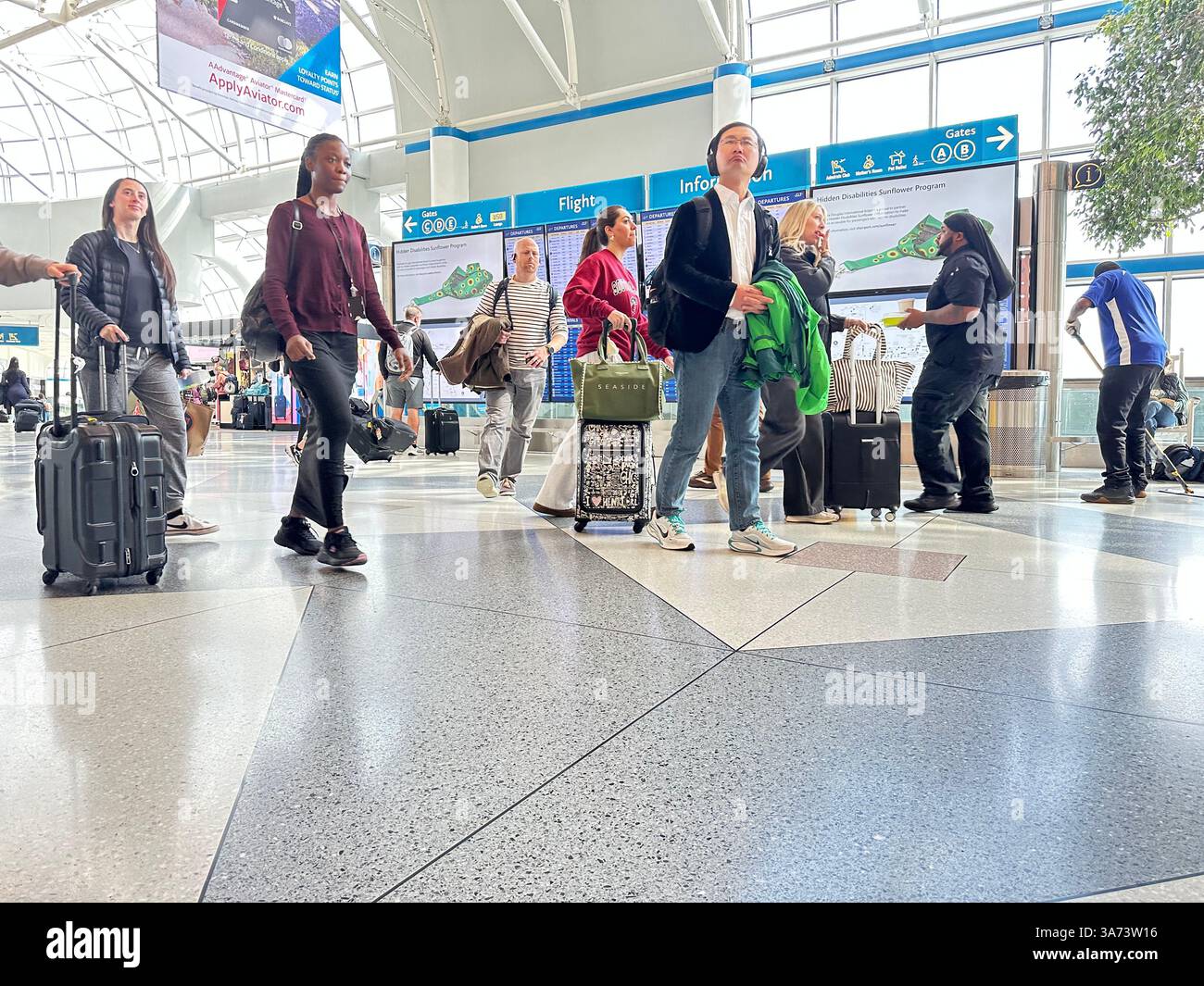 Gli Stati Uniti viaggiano con passeggeri che camminano attraverso l'atrio principale portando i bagagli oltre il tabellone informativo del volo dell'aeroporto Charlotte NC - Immagine stock catturata con smartphone