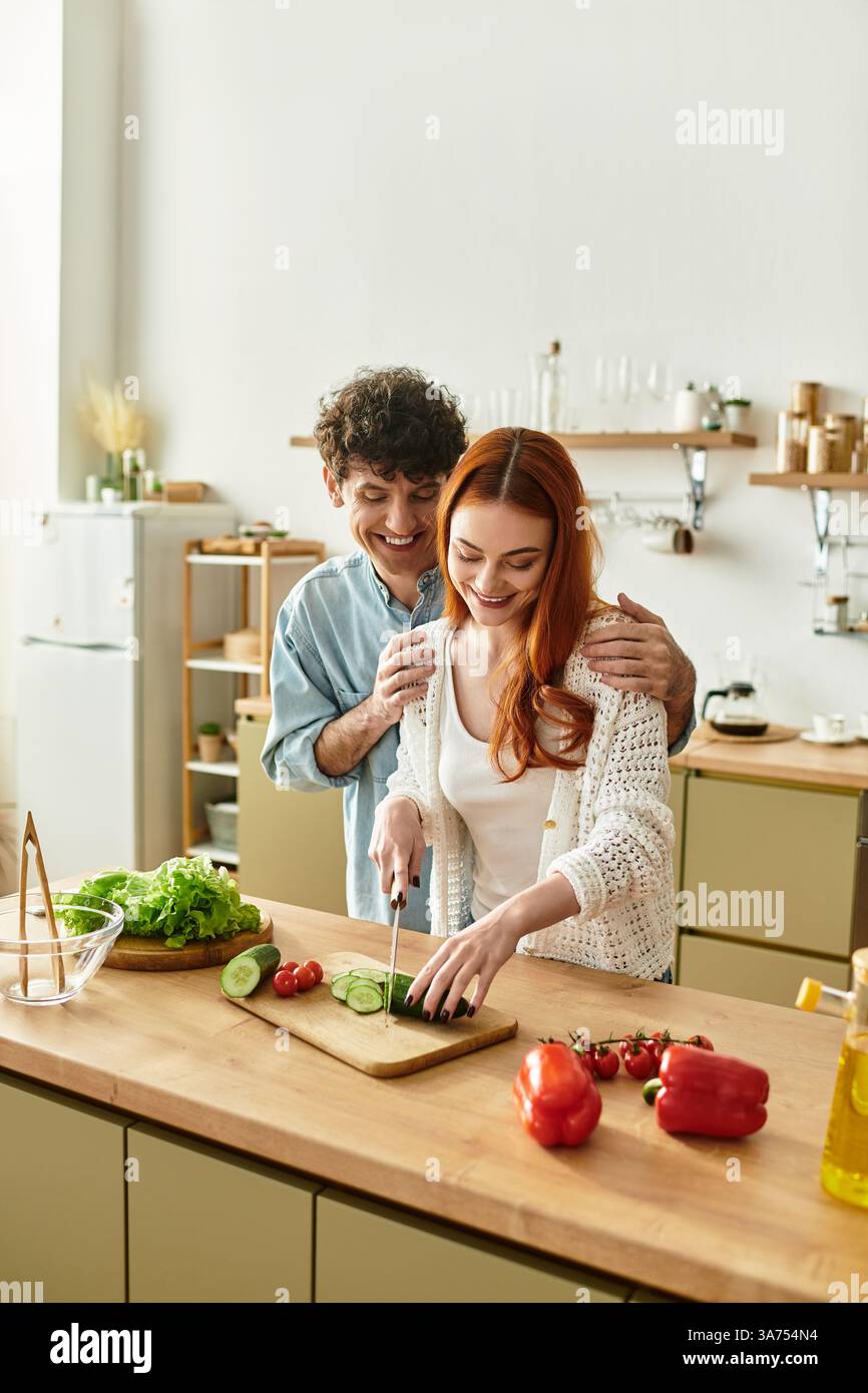 Una giovane coppia condivide un momento di gioia mentre cucinano un pasto fresco insieme, ridendo e legando. Foto Stock