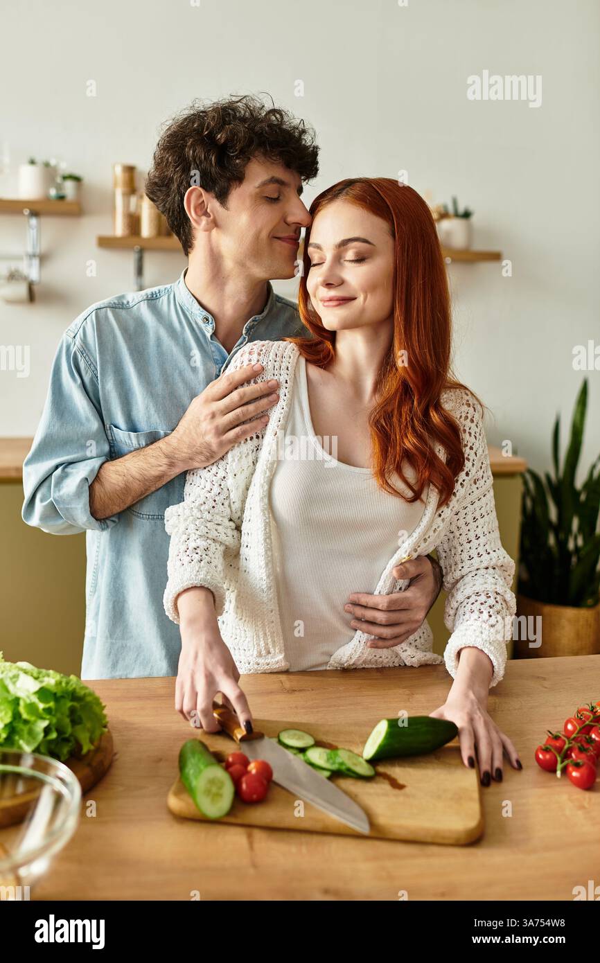 Una giovane coppia condivide un momento tenero in cucina mentre prepara un pasto fresco. Foto Stock