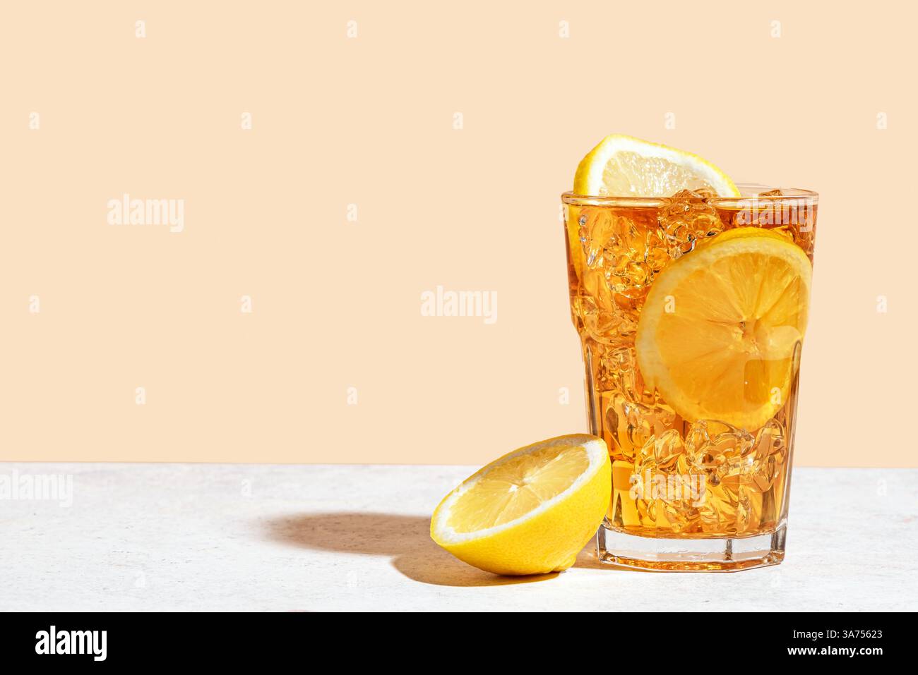 Tè ghiacciato con limone. Bicchiere di tè dolce con fette di limone e ghiaccio schiacciato su sfondo beige alla moda con luce forte, spazio copia. Estate fatta in casa c Foto Stock