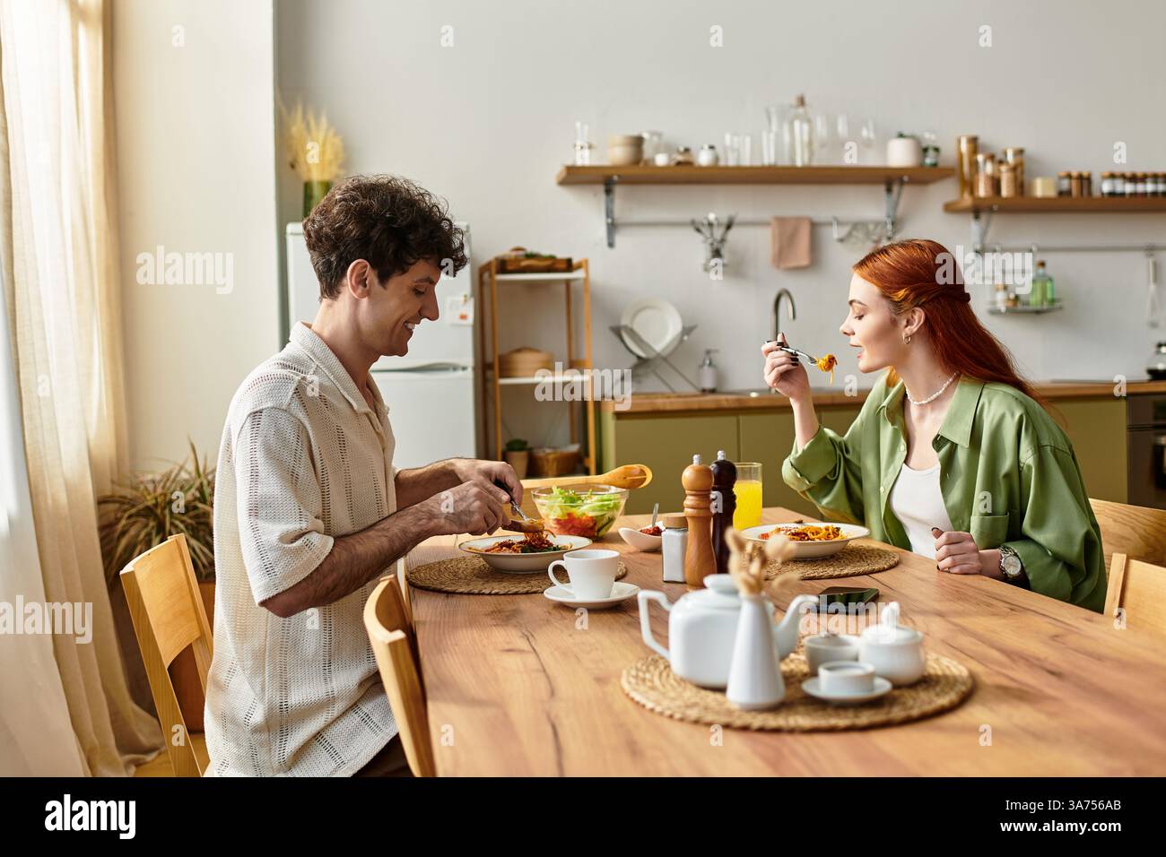 Una giovane coppia si diverte a gustare un pasto accogliente nella propria cucina, celebrando l'amore e la solidarietà. Foto Stock