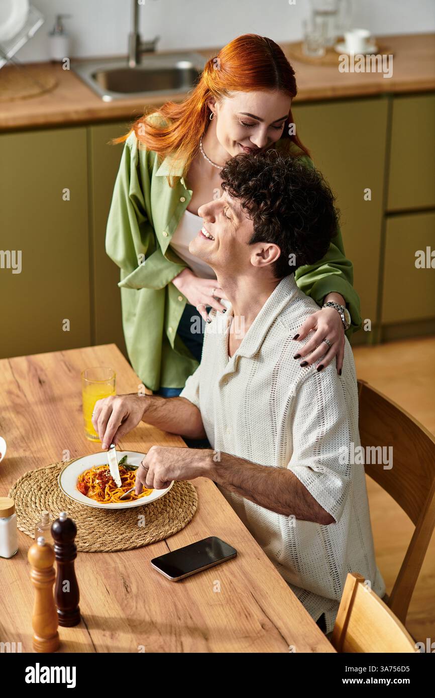 In una cucina accogliente, una giovane coppia condivide un momento di gioia mentre assapora un pasto fatto in casa. Foto Stock