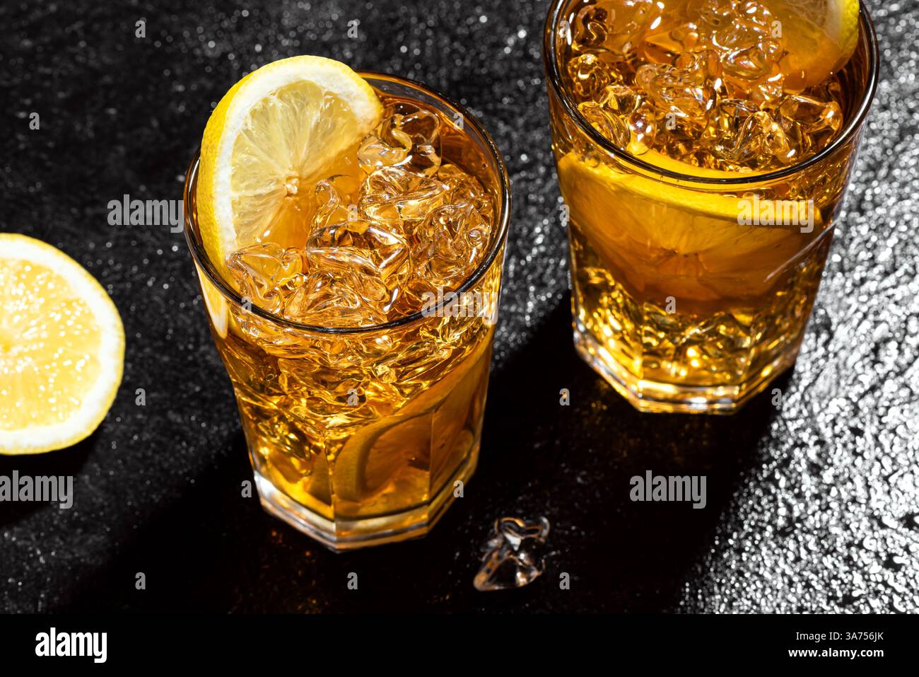 Tè ghiacciato con limone. Bicchieri di tè ghiacciato da cocktail dolce con fette di limone e ghiaccio schiantato su sfondo di ardesia nera bagnato, vista dall'alto, spazio copia. Fatti in casa Foto Stock