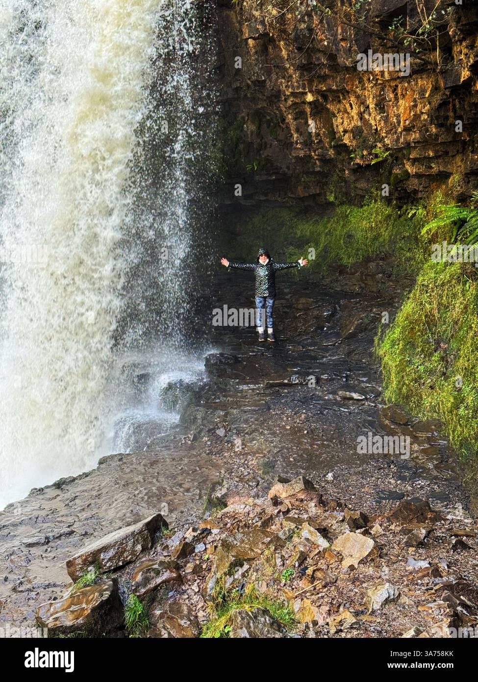 Donna sotto la cascata Sgwd Yr Eira, vale di Neath, Brecon Beacons (Bannau Brycheiniog). - Immagine stock catturata con smartphone