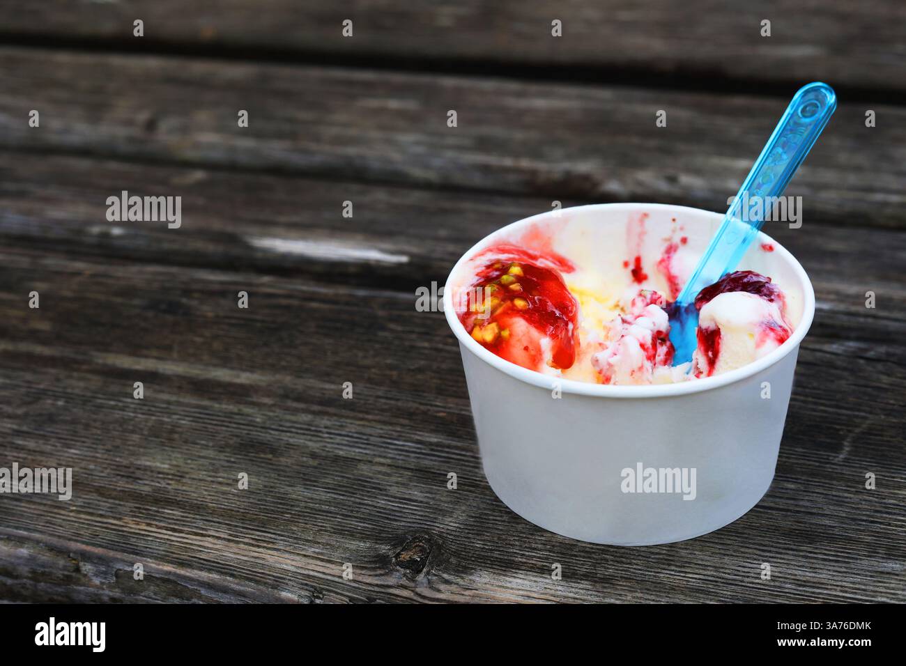 Gelato con un cucchiaio in una tazza di carta su una panca Foto Stock