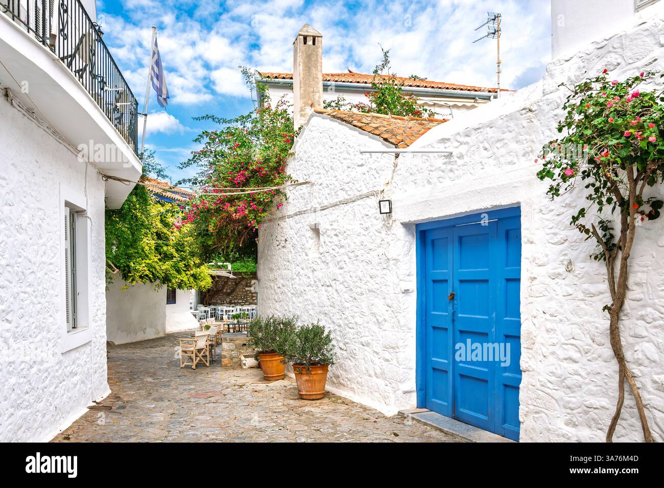 Una strada pittoresca di case imbiancate di bianco e un caffè sul marciapiede nel villaggio della piccola isola greca di Hydra, Grecia. Foto Stock