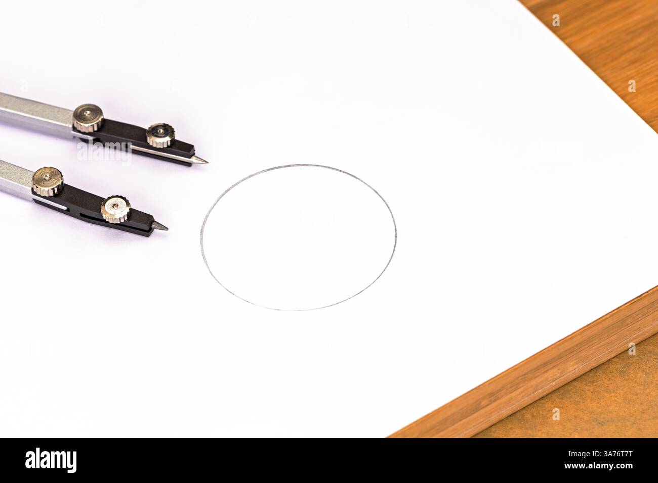 Precisione di progettazione: Primo piano di una bussola che disegna meticolosamente un cerchio perfetto su un foglio di carta pulito posizionato su un tavolo di legno marrone, trasportando la e. Foto Stock