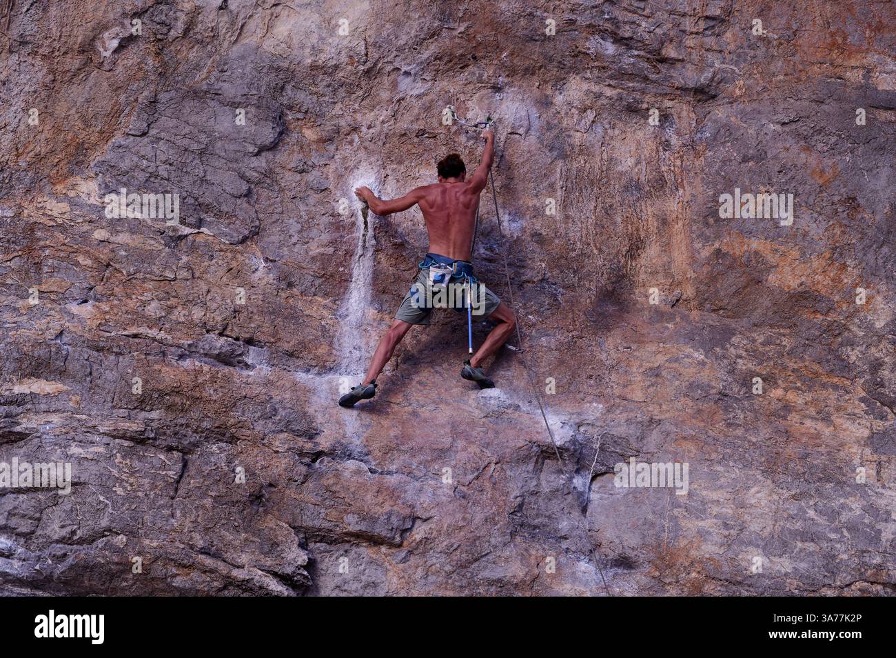 Arrampicatore concentrato che sale su una parete calcarea illuminata dal sole a Tonsai, afferrando i punti segnati da sentieri di gesso Foto Stock