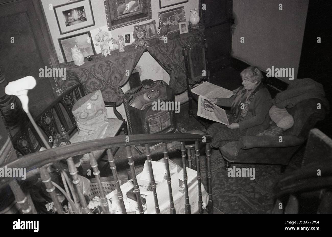 Anni '1930, la signora Cecilia Nina Bowes-Lyon, Contessa di Strathmore e Kinghorn seduta accanto a una stufa a bruciatore che legge un giornale. Membro della nobiltà britannica, era la madre della regina Elisabetta (la regina madre) e nonna della regina Elisabetta II Foto Stock