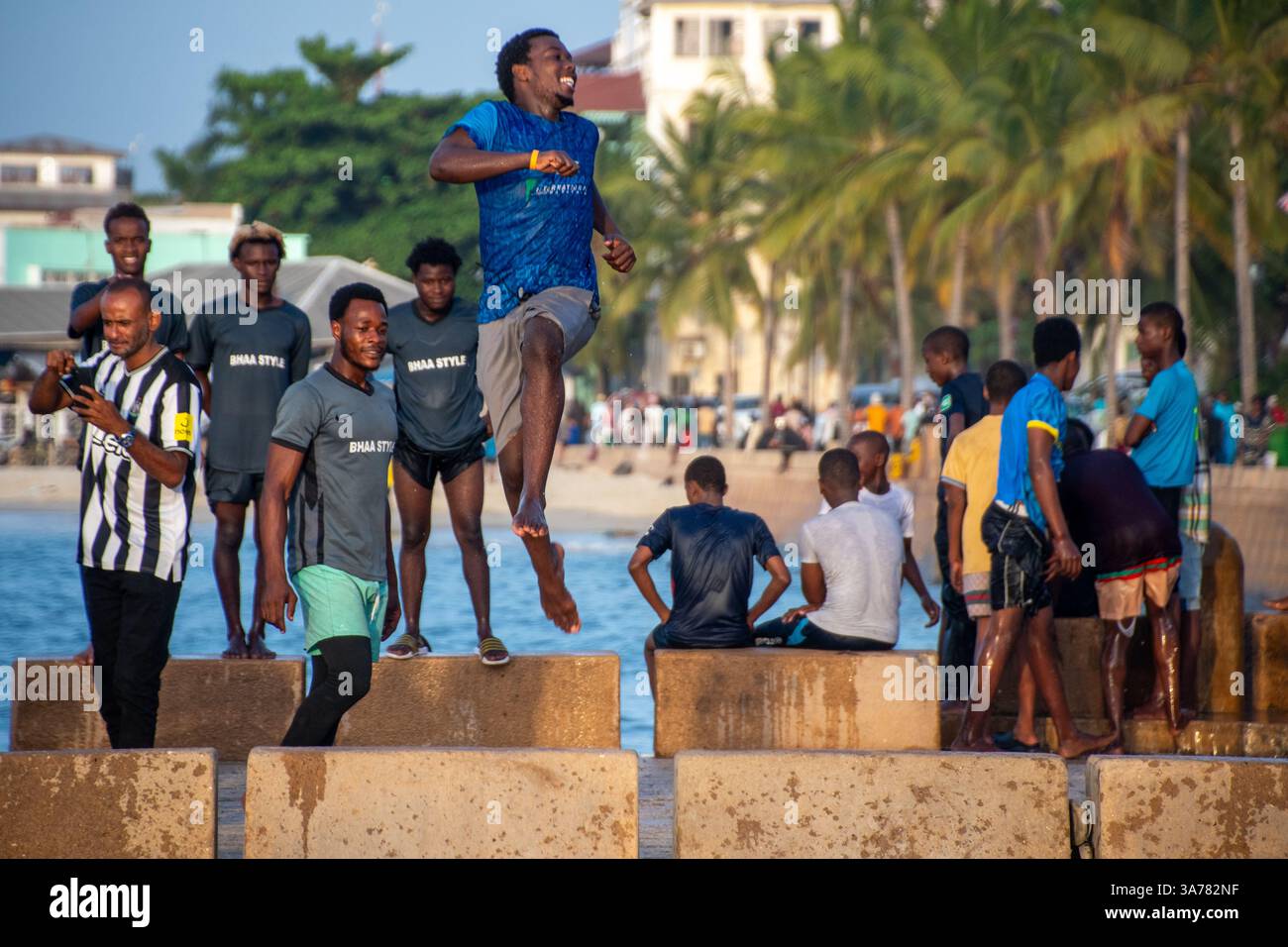I giovani si tuffano con gioia da un molo di pietra nell'oceano di Zanzibar, Tanzania Foto Stock