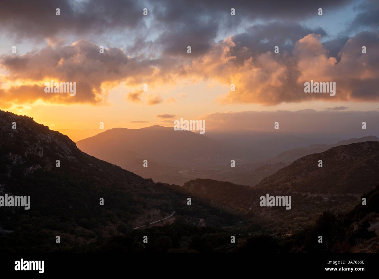 Ecco una didascalia per l'immagine: **L'ora d'oro bagna il paesaggio montuoso con un caldo bagliore mentre il sole tramonta, dipingendo le nuvole con sfumature di oranghi Foto Stock