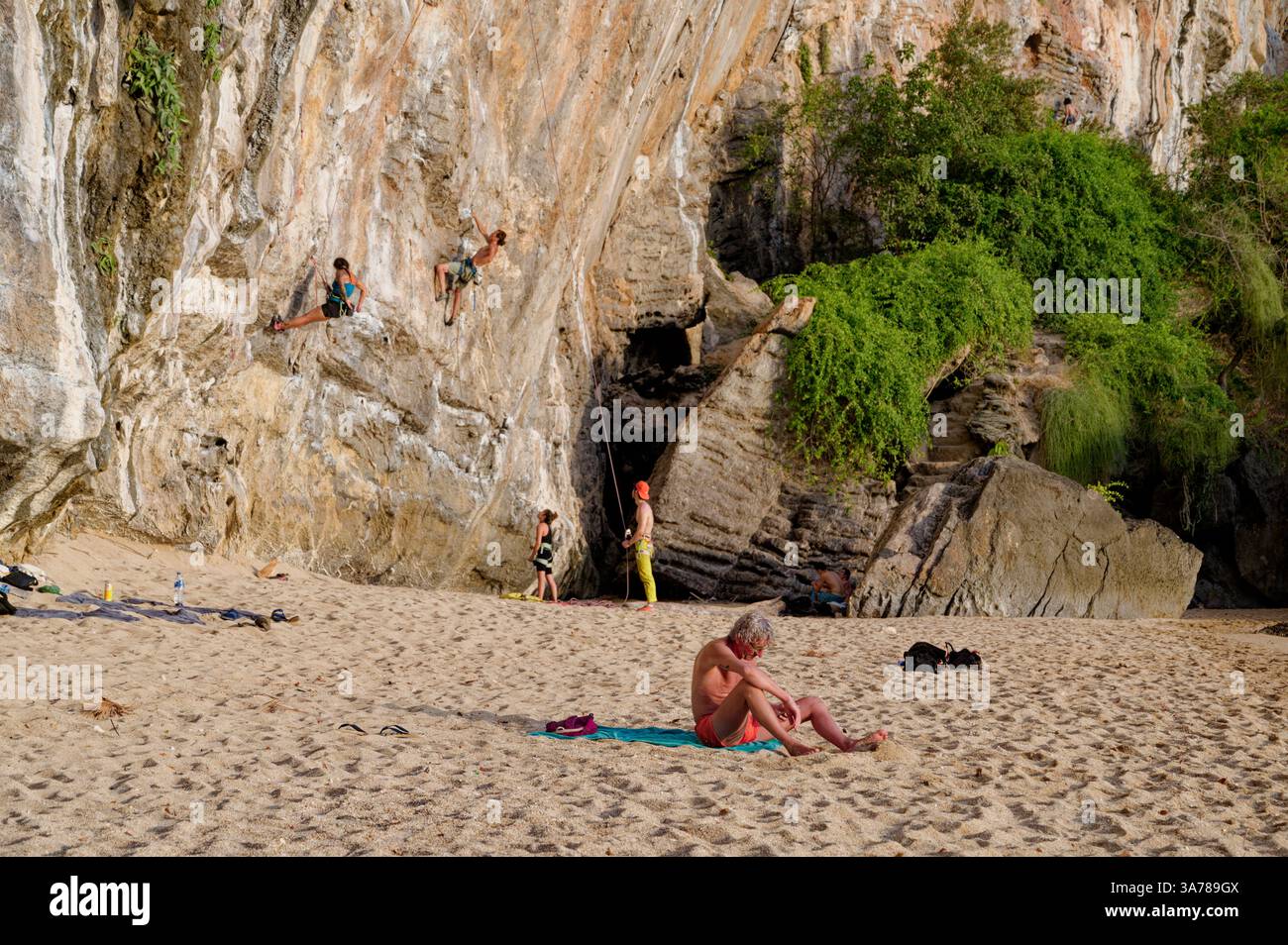 Gli arrampicatori scalano una scogliera calcarea sulla spiaggia di Tonsai, mentre un belvedere tiene d'occhio e un bagno di sole si rilassa sulla sabbia Foto Stock