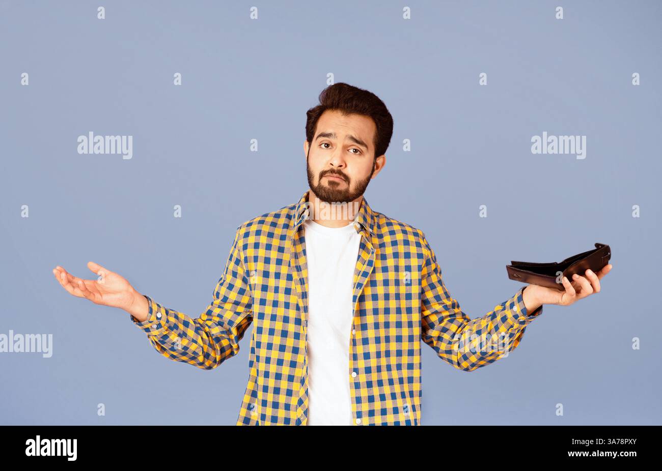 Crisi economica e bancarotta. Un ragazzo indiano sconvolto con un portafoglio vuoto che le spalle si infrangono su sfondo viola Foto Stock