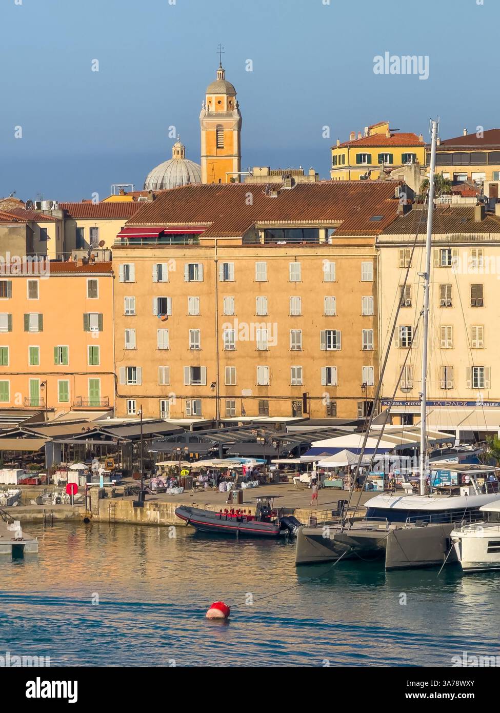 Ajaccio, Corsica, Francia 8 luglio 2024: Lungomare del porto con la cattedrale di Santa Maria Assunta che torreggia su un edificio a più piani. Barche attraccate Foto Stock