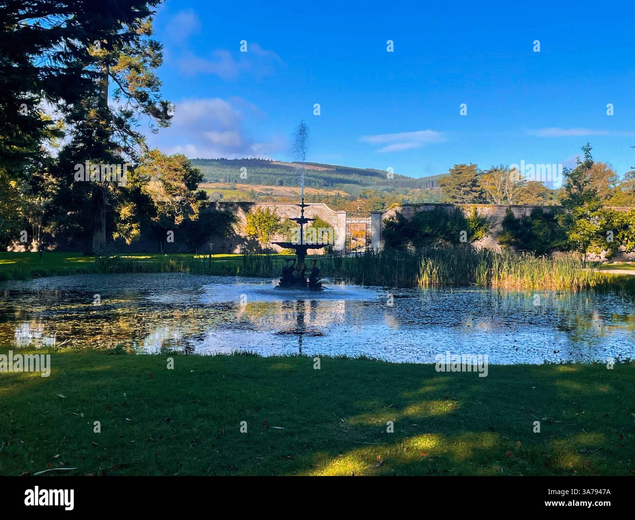 Tranquillo giardino con fontana e laghetto adagiato contro pareti di pietra e colline lontane in Irlanda. Foto Stock