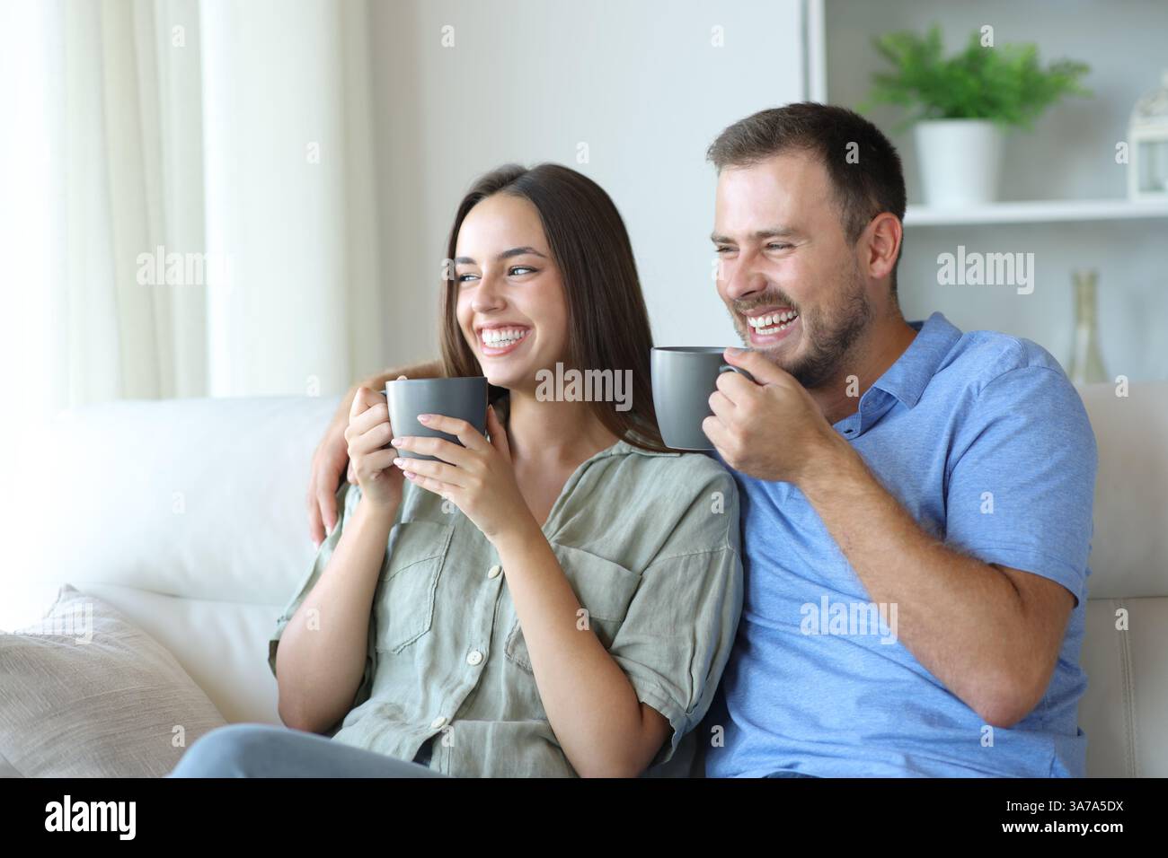 Coppia felice sorridente e bevendo un caffè seduto su un divano a casa Foto Stock