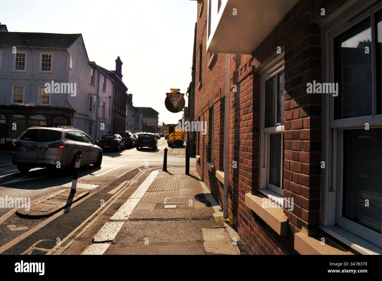 Scena stradale a metà pomeriggio, forte luce e ombra ambulanza stazionaria, segnaletica per cedere. Foto Stock