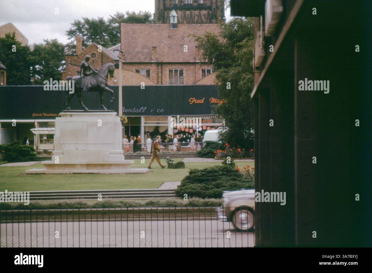 Una fotografia d'archivio degli anni '1960 dell'iconica statua di Lady Godiva a Broadgate, Coventry, West Midlands. Ripresa su pellicola da 35 mm, questa scena d'epoca presenta la statua in una vivace area commerciale con i negozi Bendall & Co. E Fred Mayne sullo sfondo, insieme a un'auto d'epoca e a un giardiniere che si occupa del prato. Foto Stock